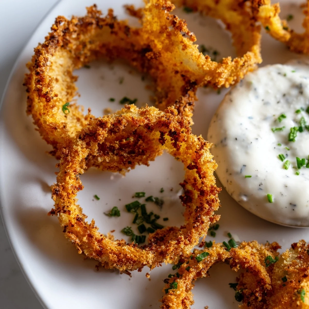 Freshly baked Crispy Baked Onion Rings stacked high, golden brown and crunchy, served next to a small bowl of creamy homemade ranch dressing for dipping.