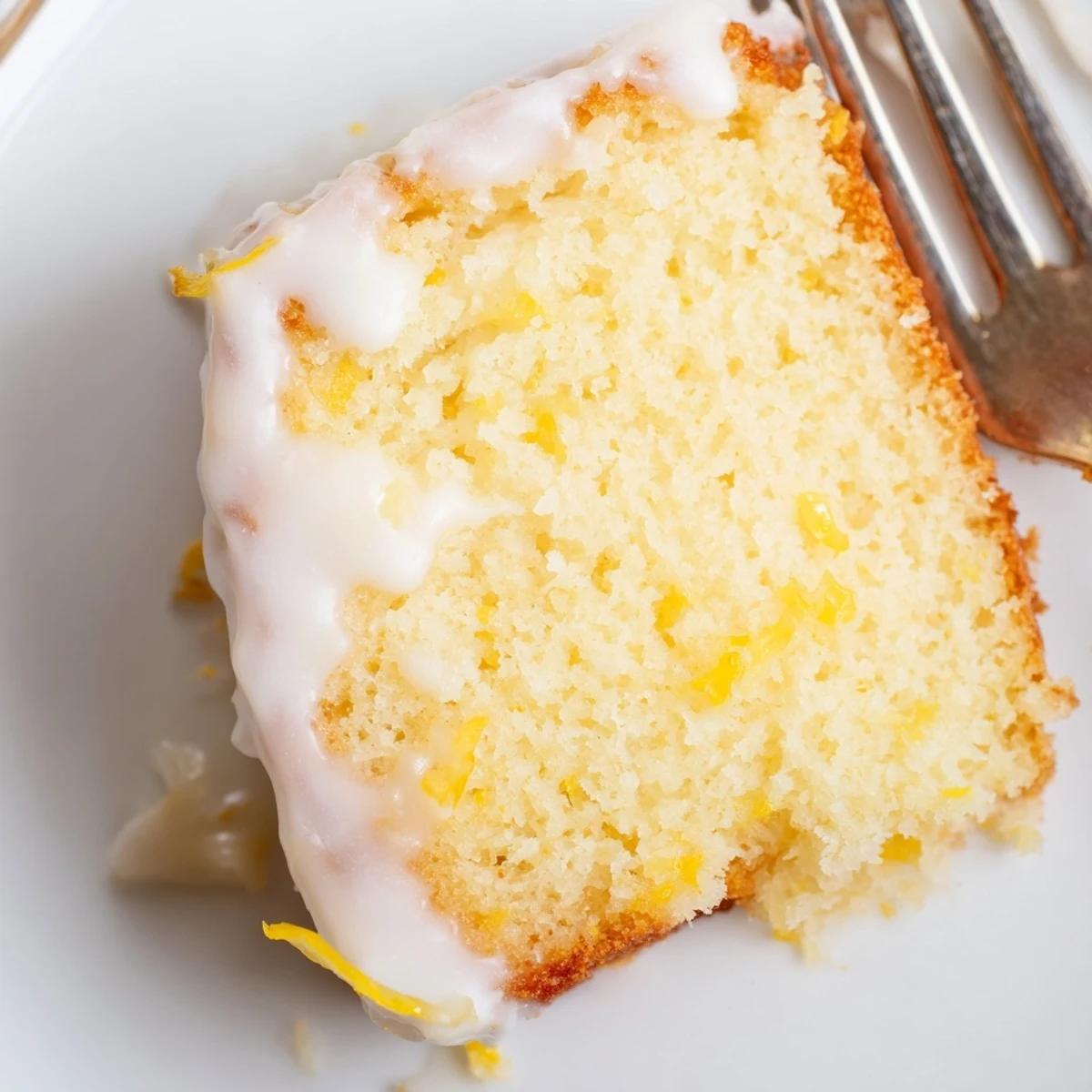 Moist slice of Lemon Loaf with Glaze served on a white plate with tea.