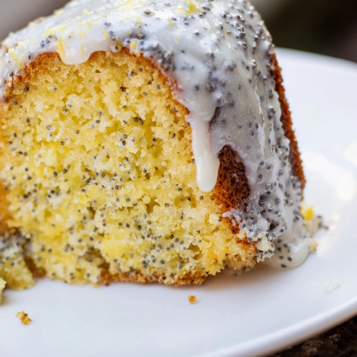 Lemon Poppy Seed Bundt cake on a white platter, garnished with fresh lemon slices and powdered sugar.