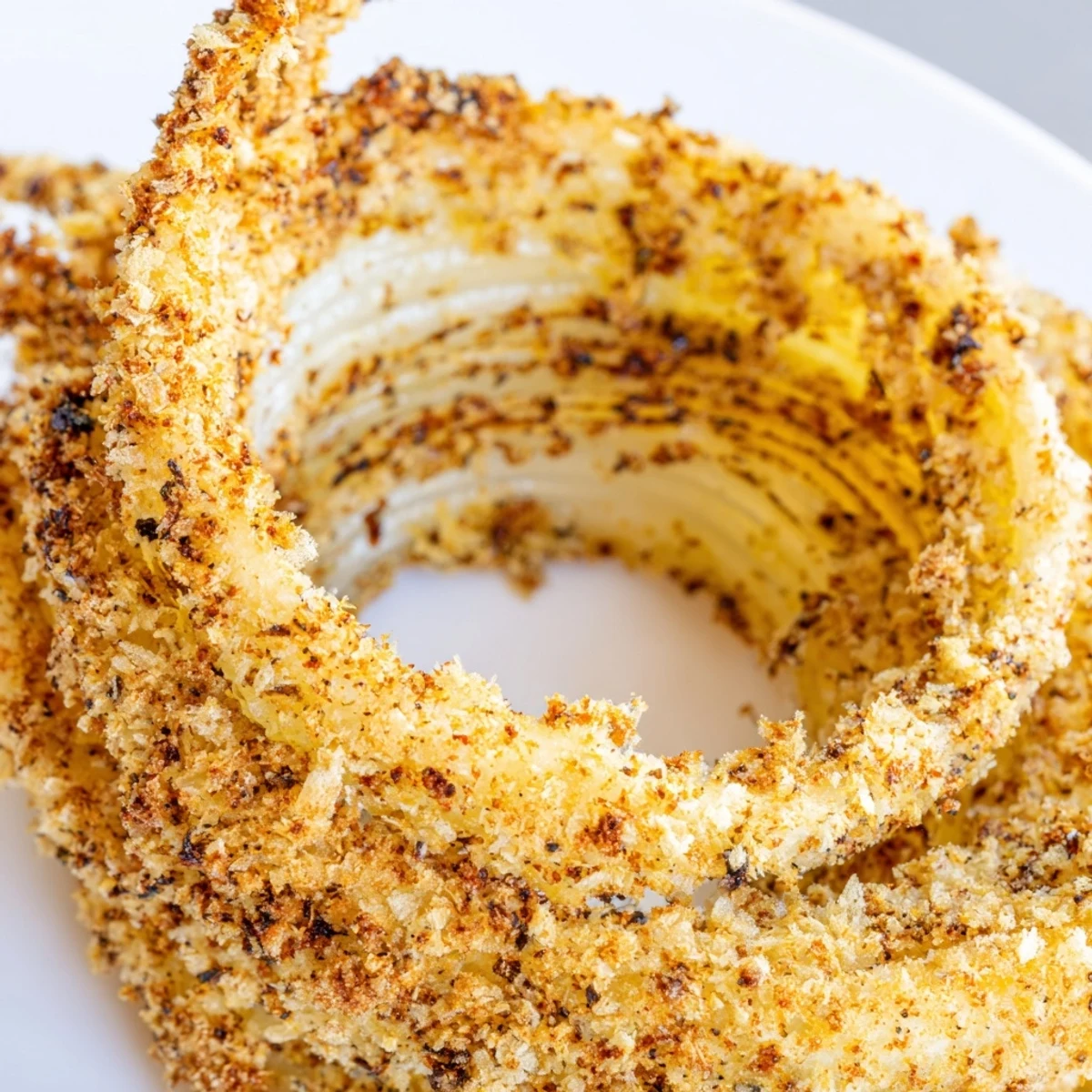 Stack of golden Crispy Baked Onion Rings next to a cheeseburger for a delicious snack platter.