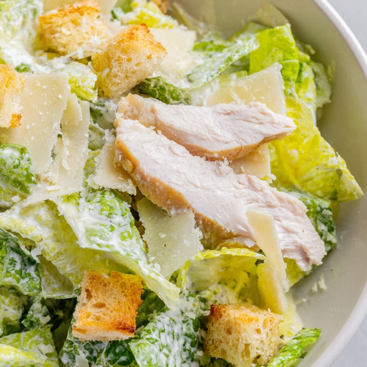 A close-up of a vibrant Chicken Caesar Salad with juicy grilled chicken, creamy Caesar dressing, and golden croutons on a rustic table.