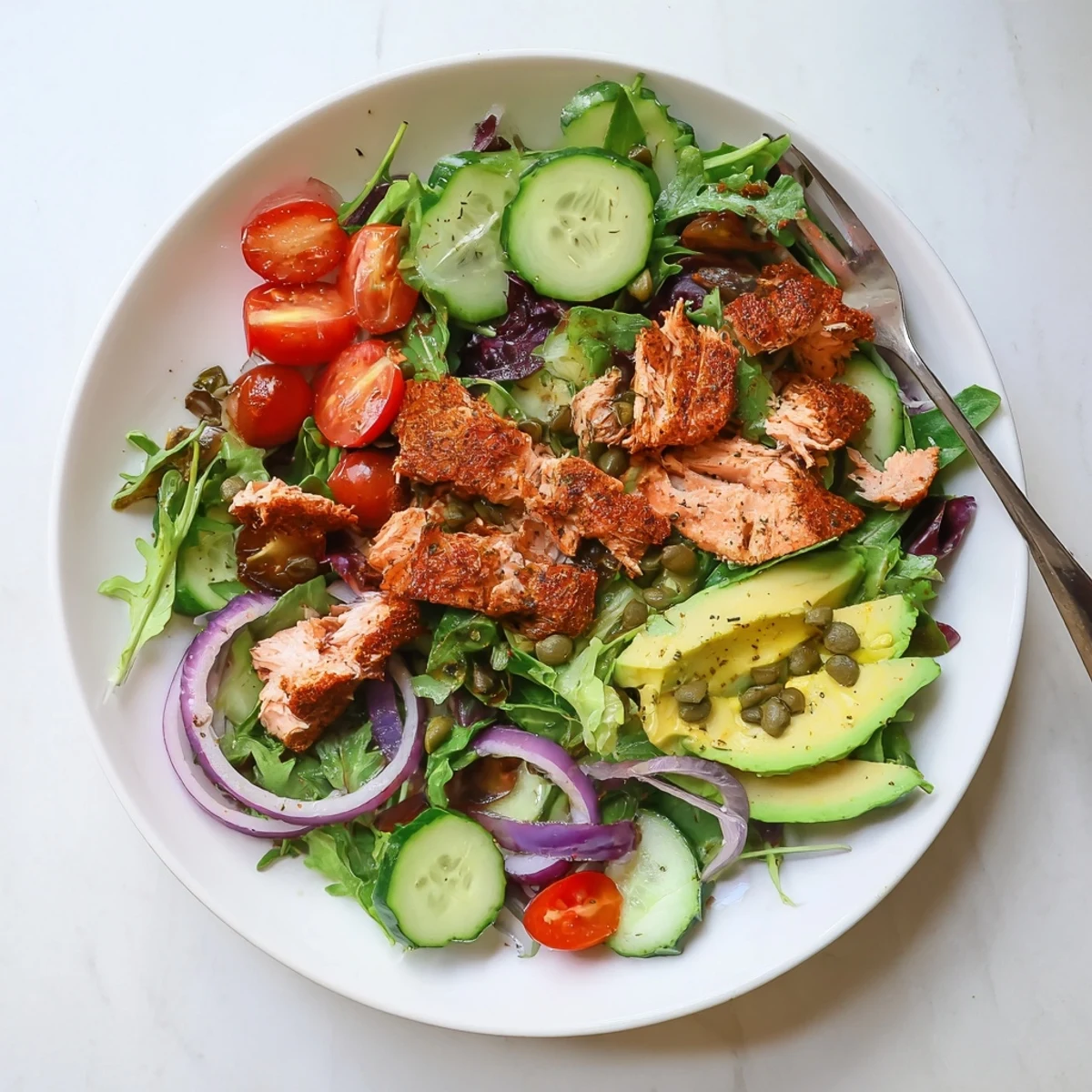 A close-up of a plated Baked Salmon Lunch Salad with flaked salmon, avocado slices, and cherry tomatoes on mixed greens, drizzled with lemon-dill vinaigrette.
