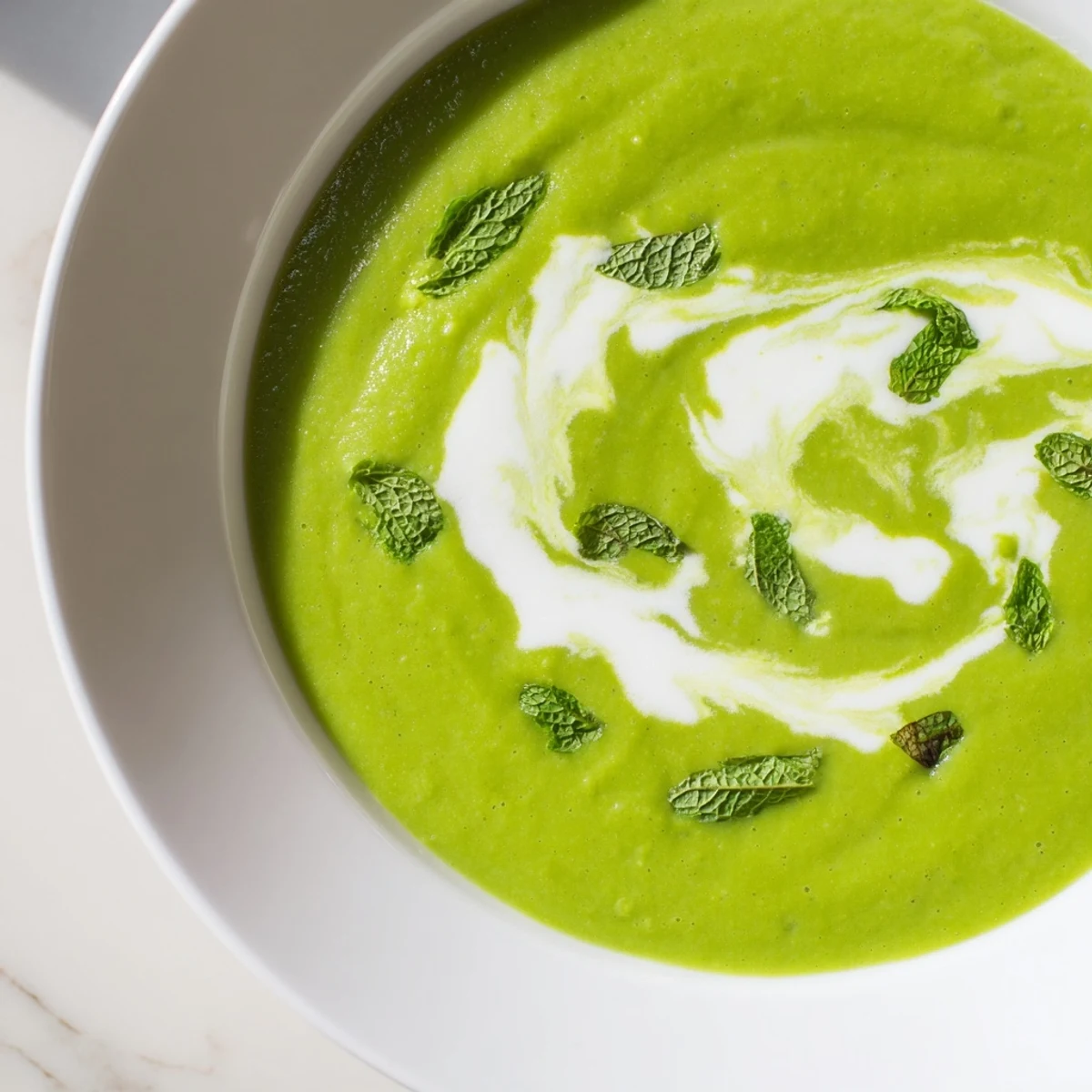 Creamy Green Pea and Mint Soup garnished with fresh mint leaves and a drizzle of heavy cream.