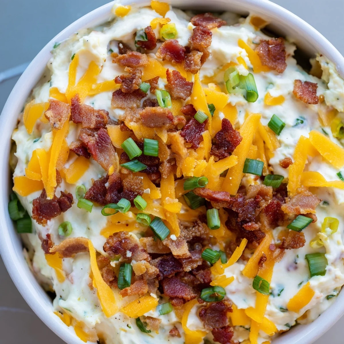 A chilled scoop of Super Bowl Loaded Baked Potato Dip next to crunchy potato chips and waffle fries for game day.