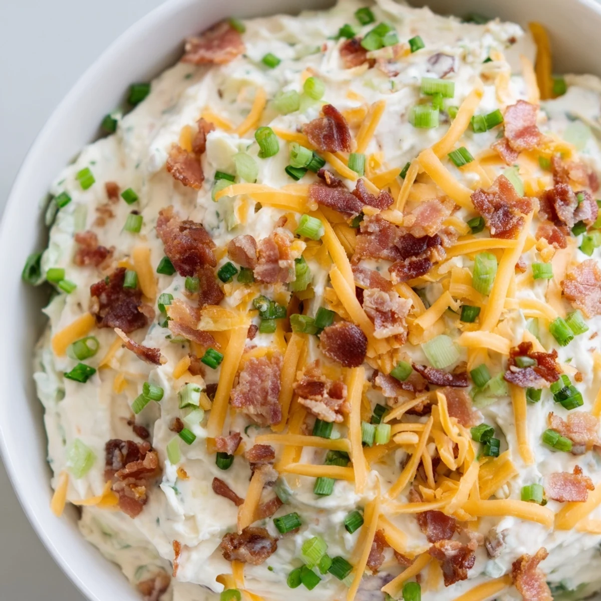 Rich and tangy Super Bowl Loaded Baked Potato Dip topped with shredded cheddar cheese and green onions on a platter.