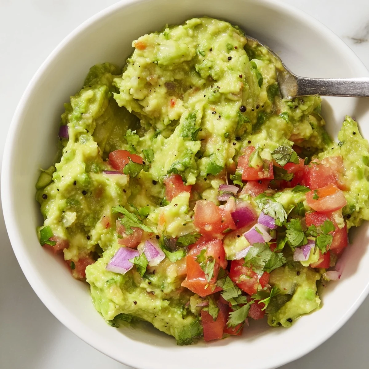 Freshly made guacamole with chunky pico de gallo salsa, served in a white bowl with lime wedges and vibrant tomatoes.