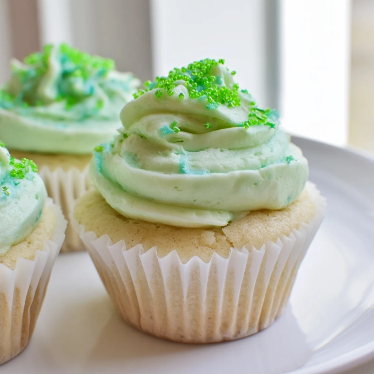 Close-up of Shamrock Shake Cupcakes with Mint Frosting, showing fluffy vanilla cupcakes topped with creamy, vibrant green frosting and festive sprinkles for St. Patrick's Day.