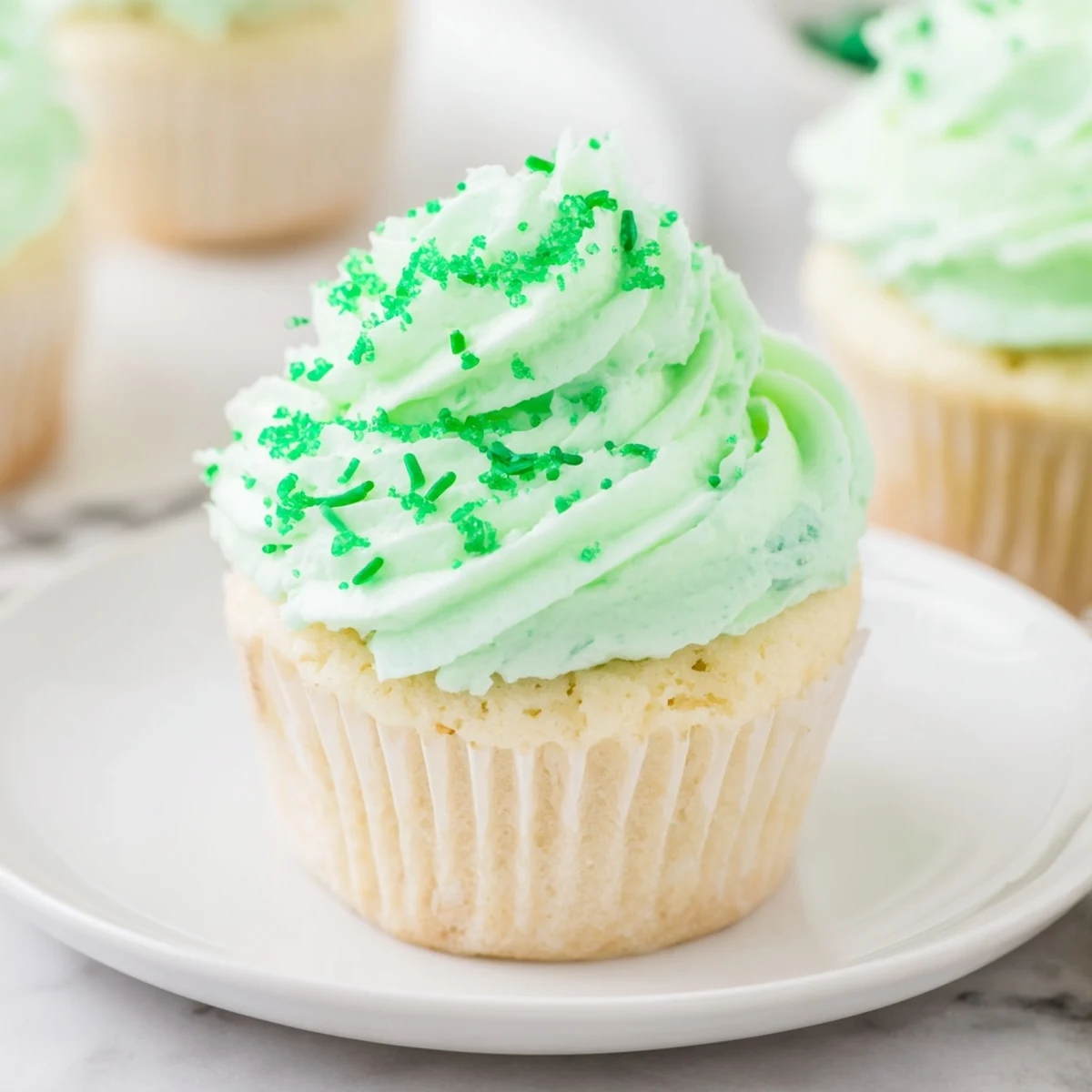 A dozen Shamrock Shake Cupcakes with Mint Frosting arranged on a marble board, their minty green swirls glistening and ready to serve with a glass of cold milk.