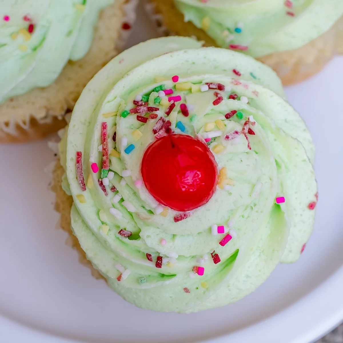 A close-up view showcases Shamrock Shake Cupcakes, with creamy mint frosting piped high and a mini straw nestled beside the cupcake.