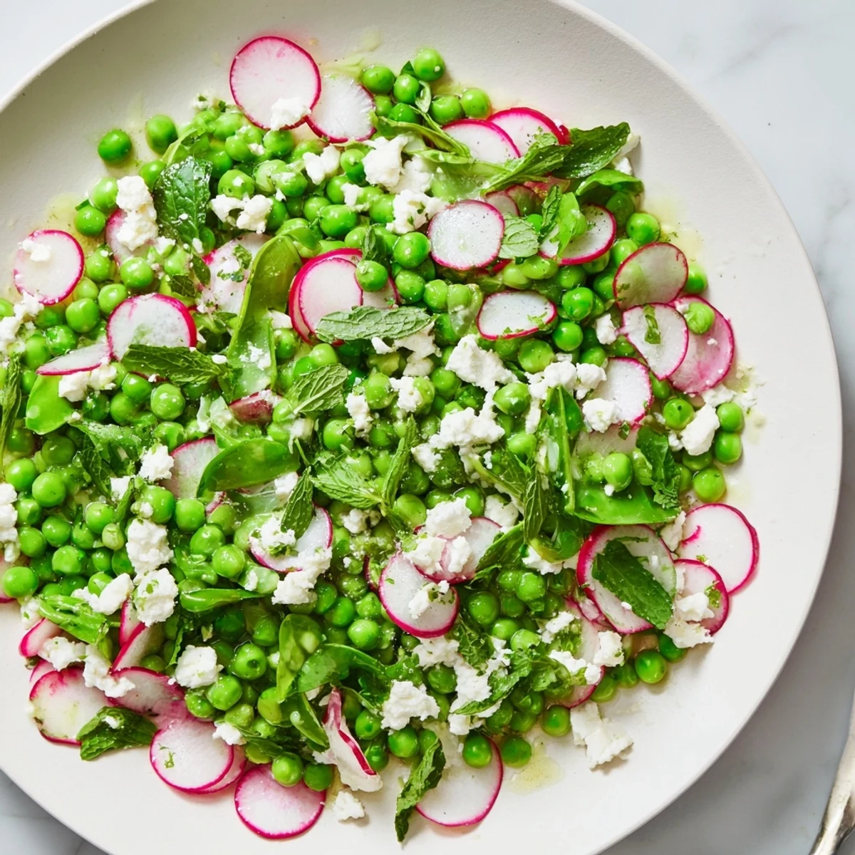 A vibrant Spring Pea Salad with Radishes and Feta, garnished with mint and ready for a spring gathering.  