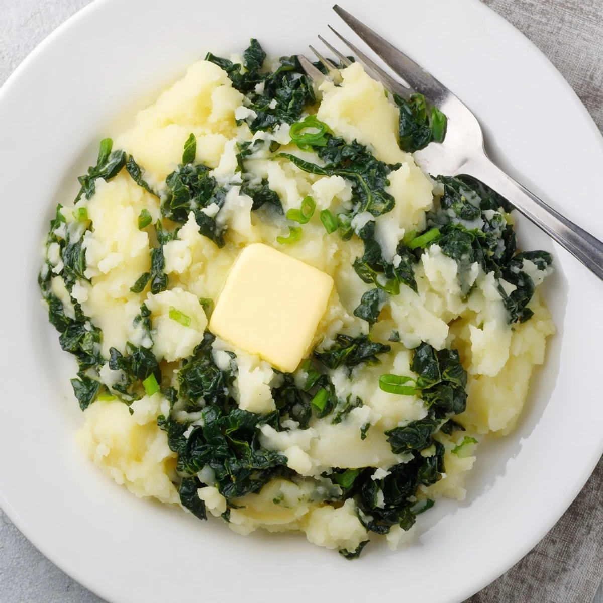 A close-up of Irish Colcannon with golden butter pooled in the center, showcasing vibrant green kale and scallions mixed into smooth, fluffy mashed potatoes.