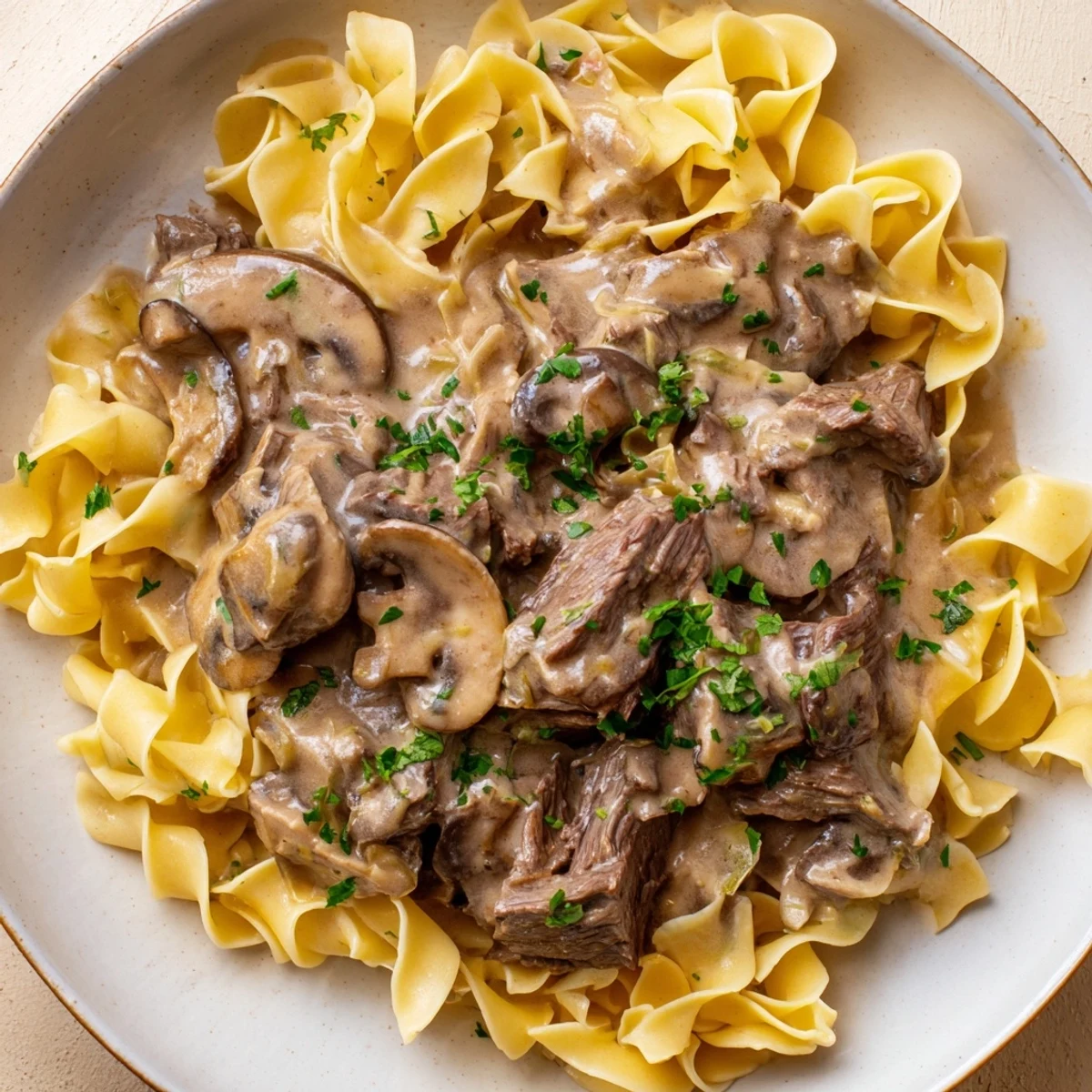 Steaming Beef Stroganoff with Mushroom Gravy served over buttery egg noodles and garnished with fresh parsley.