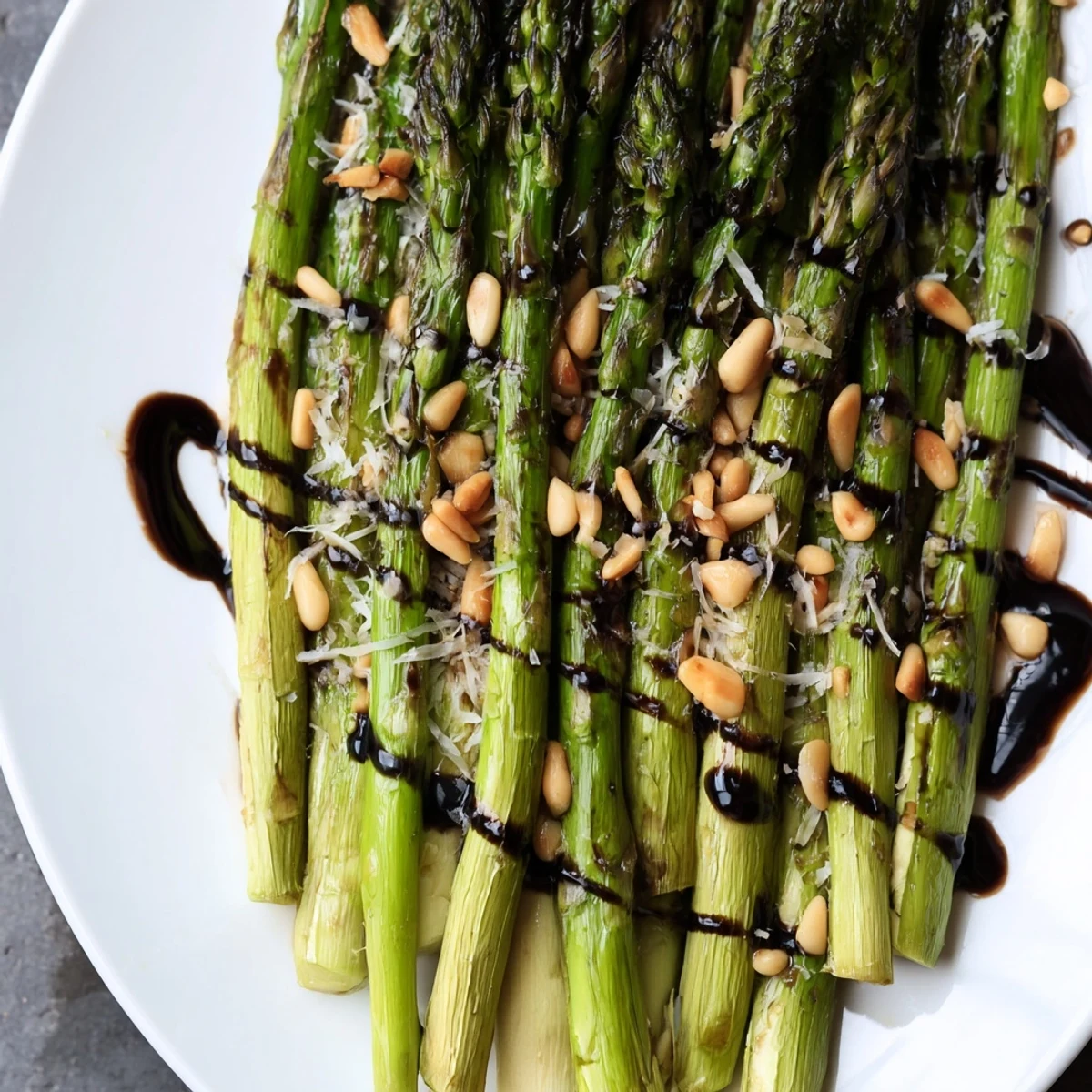 Roasted asparagus with balsamic reduction garnished with pine nuts on platter.