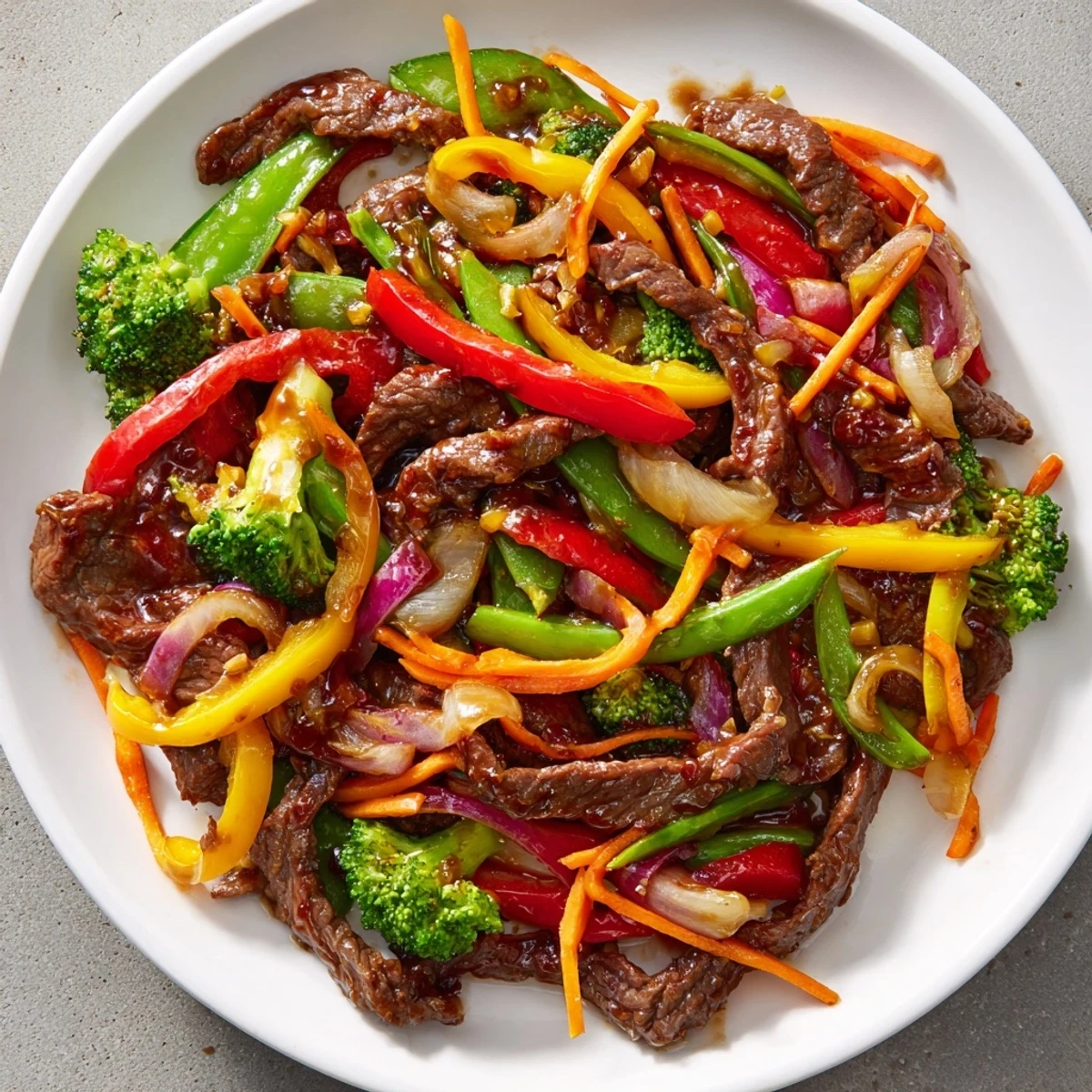 Sizzling Spicy Beef Stir Fry with Mixed Vegetables on a plate next to steamed white rice, highlighting the tender beef and crunchy snap peas.