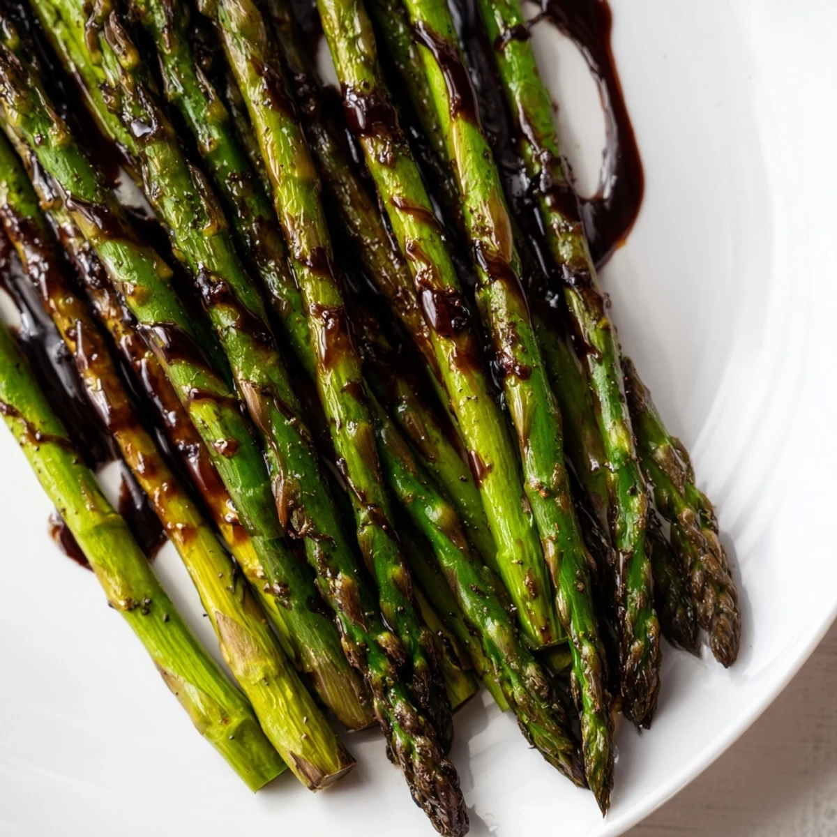 Tender roasted asparagus spears topped with sweet balsamic glaze, served warm on a wooden table.