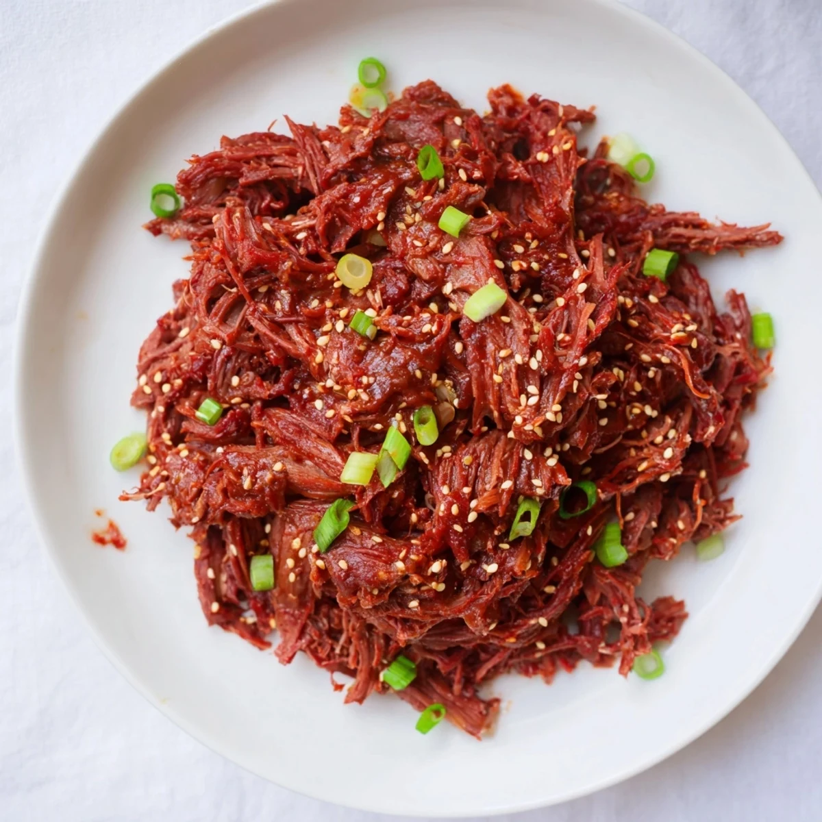 Fork-tender shredded Slow Cooker Korean Beef with a savory-sweet glaze, paired with kimchi and steamed vegetables for a complete meal.