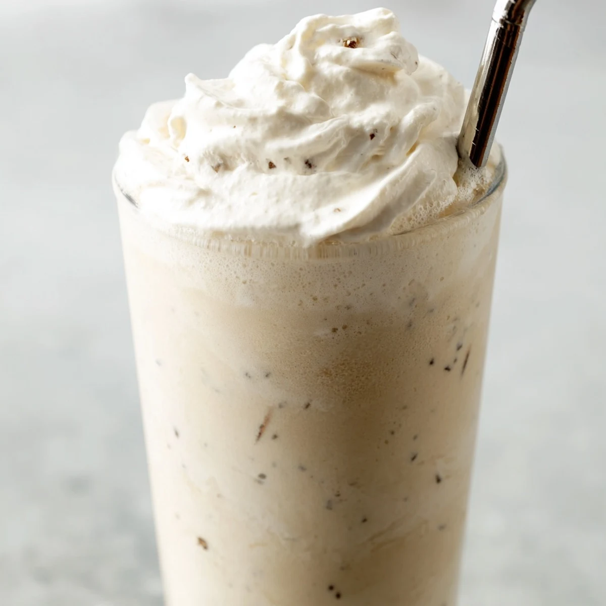 A tall glass of Vanilla Bean Frappuccino topped with fluffy whipped cream and a straw.