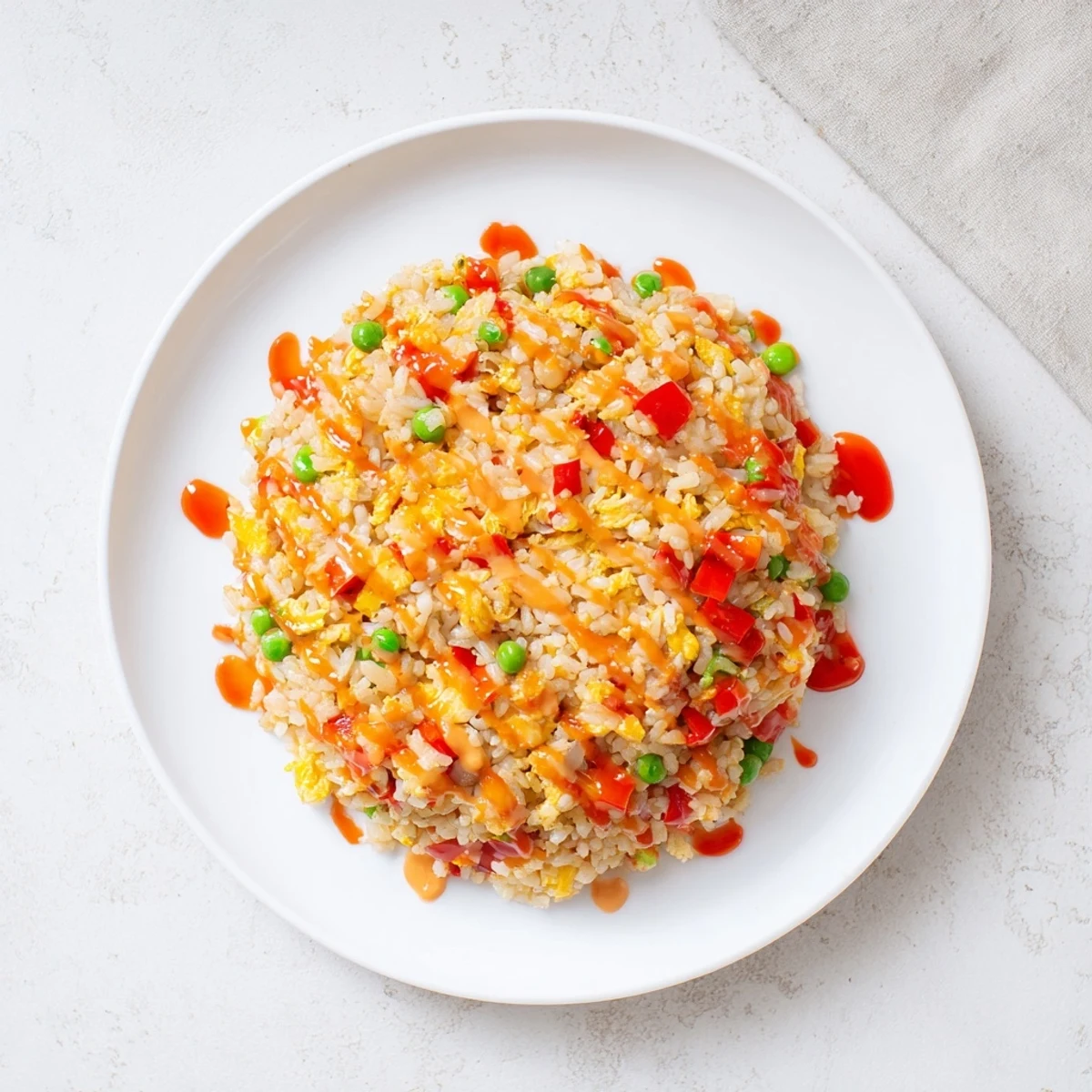 A close-up of vibrant Bang Bang Fried Rice with red peppers, peas, and creamy drizzle.