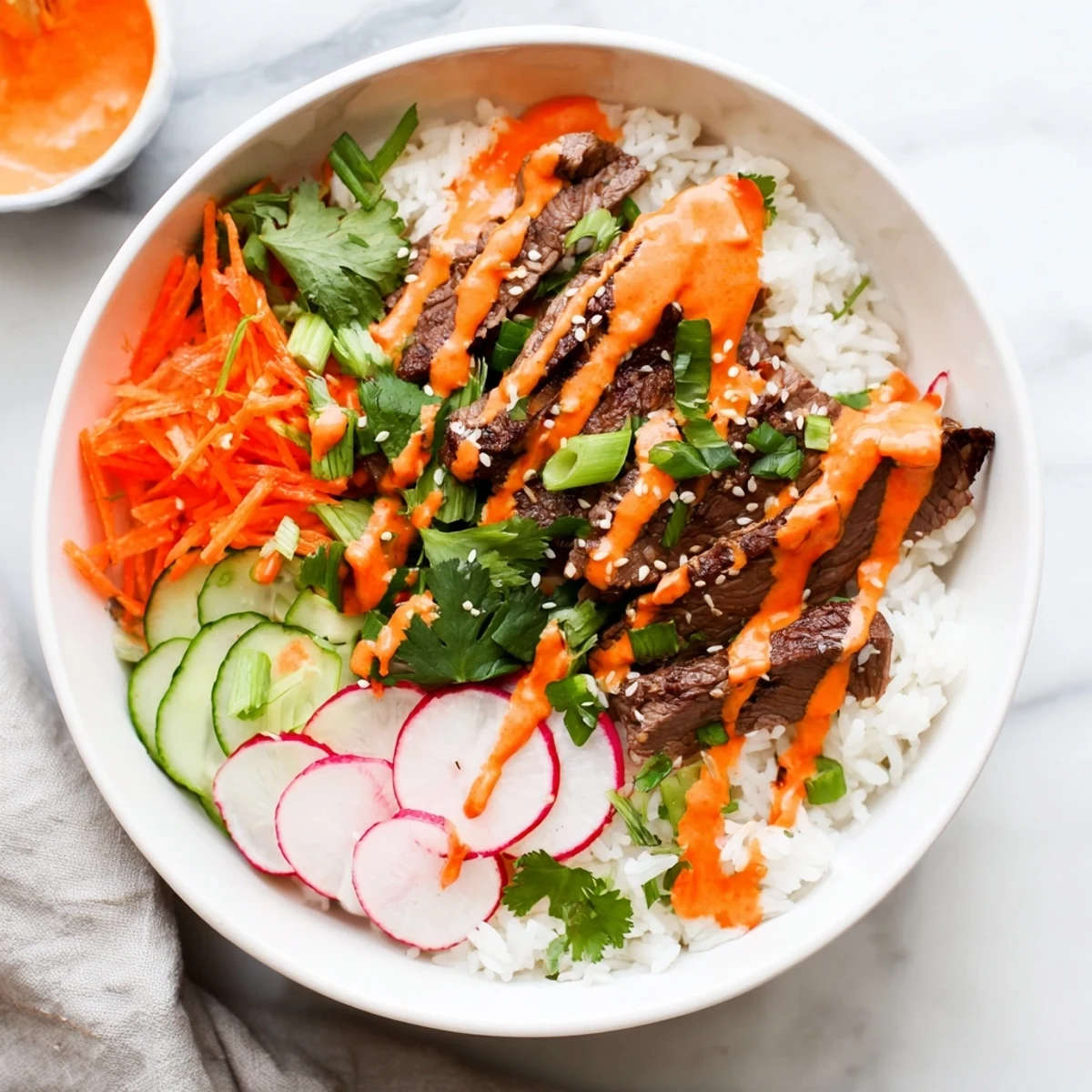Close-up photo of juicy marinated steak over steamed rice, loaded with crunchy veggies and a creamy, spicy gochujang sauce.
