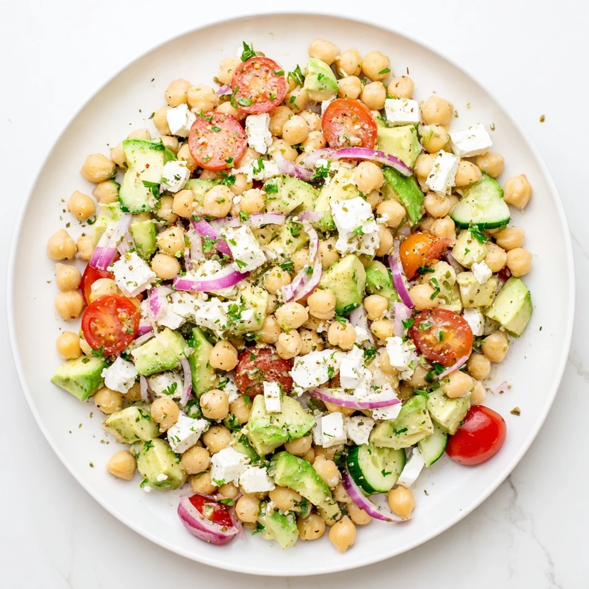 A vibrant Chickpea Feta Avocado Salad with diced cucumber and red onion, drizzled with a zesty lemon dressing in a bowl.