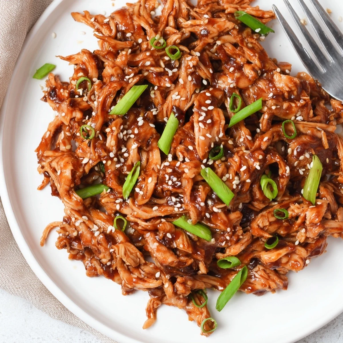 Slow cooker Mongolian chicken featuring shredded tender pieces coated in a glossy brown garlic sauce over fluffy white rice