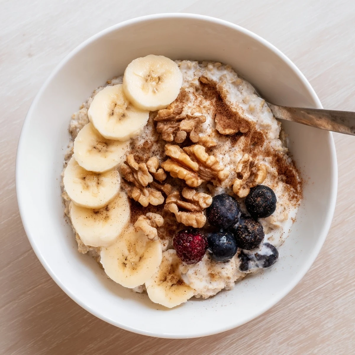 Spoon lifting thick cinnamon-spiced brown sugar overnight oats from a white bowl with berries on top