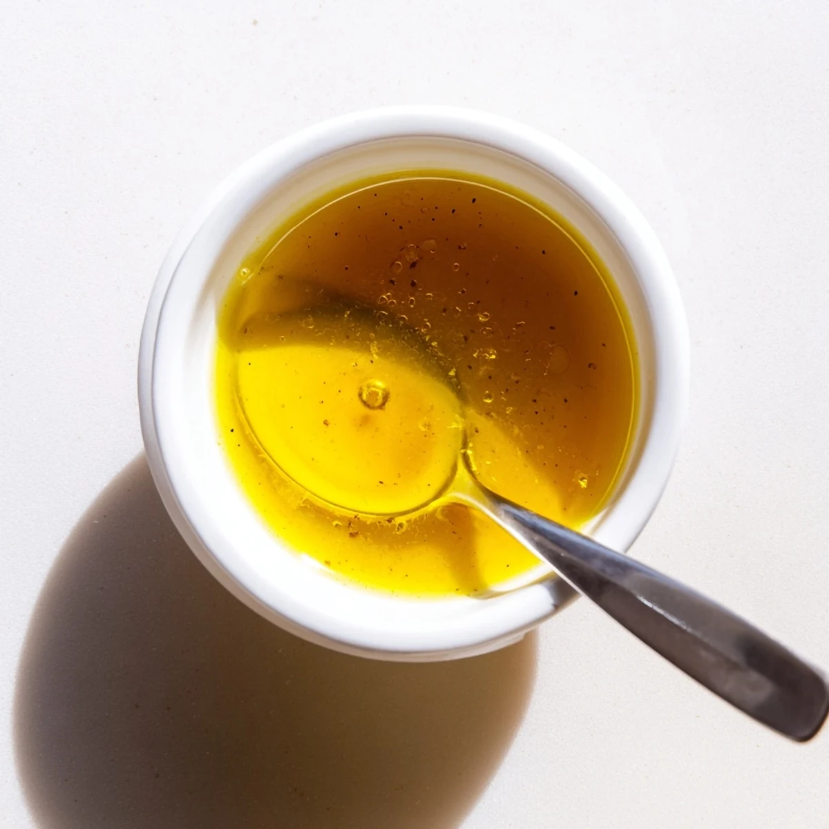 Golden honey lemon vinaigrette drizzled over fresh mixed greens in a white bowl