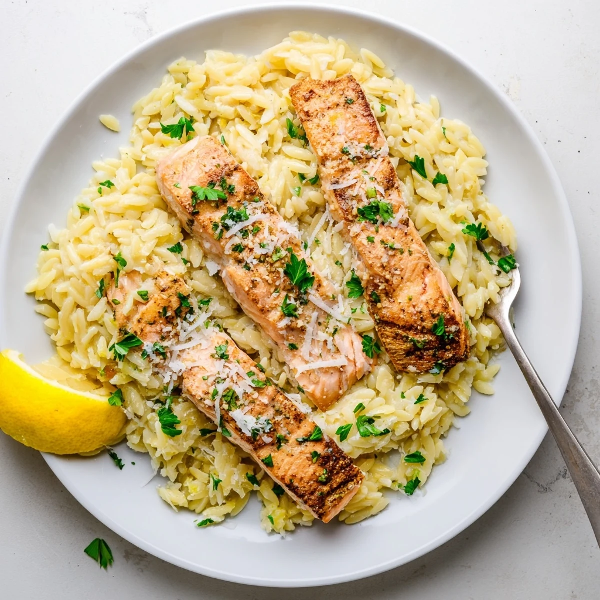 Golden seared salmon fillets resting atop creamy lemon orzo in a cast iron skillet