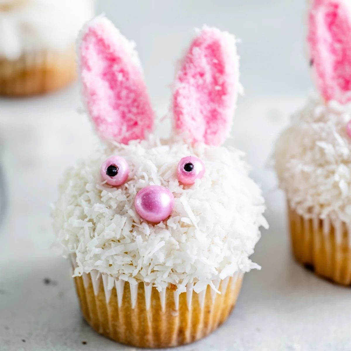 Easter bunny cupcakes decorated with white coconut, pink sugar-dusted ears, and jelly bean noses
