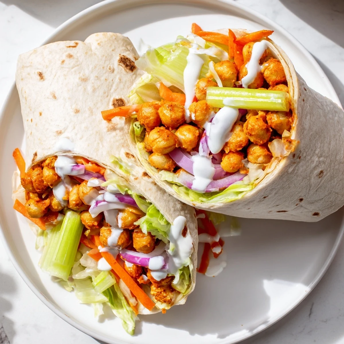 Vibrant buffalo chickpea wraps sliced in half revealing seasoned chickpeas, crunchy carrots, and celery