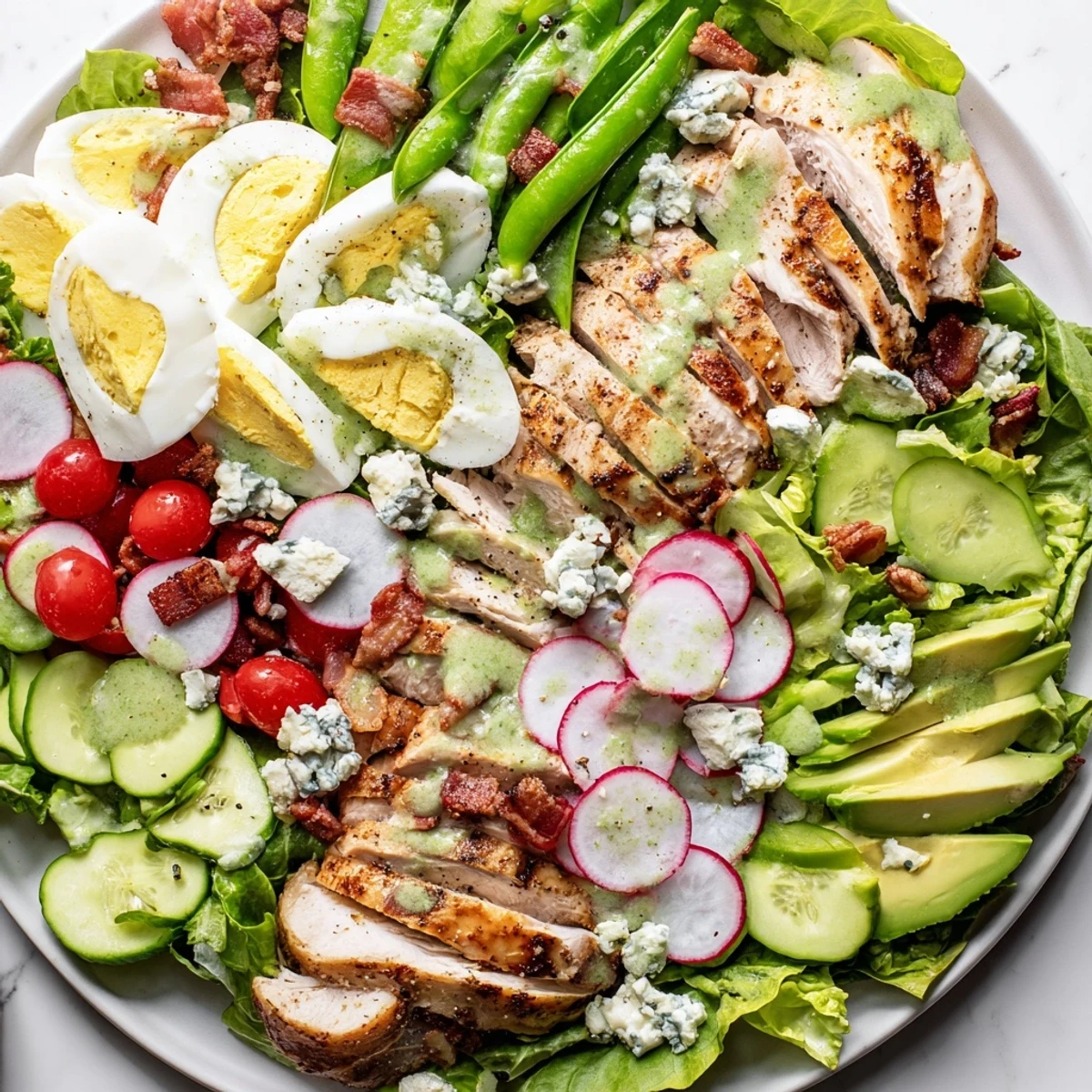 Colorful Spring Cobb Salad arranged with grilled chicken, eggs, bacon, avocado, and crisp vegetables drizzled with herb vinaigrette