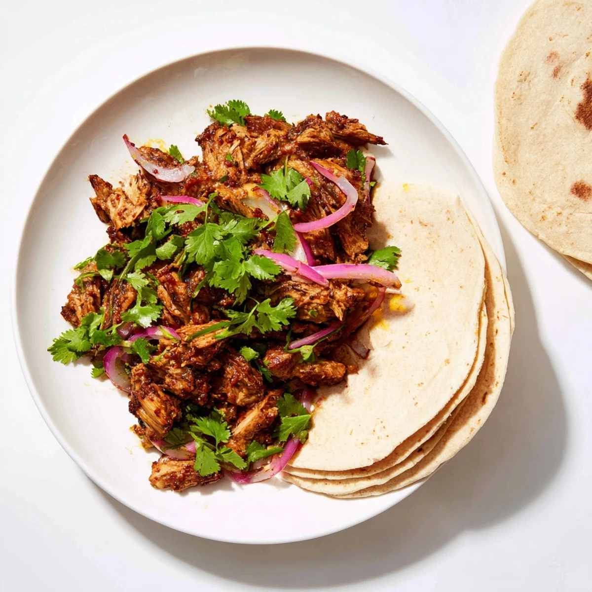 Golden brown shredded vegan carnitas with mushrooms piled in a serving bowl with fresh cilantro garnish