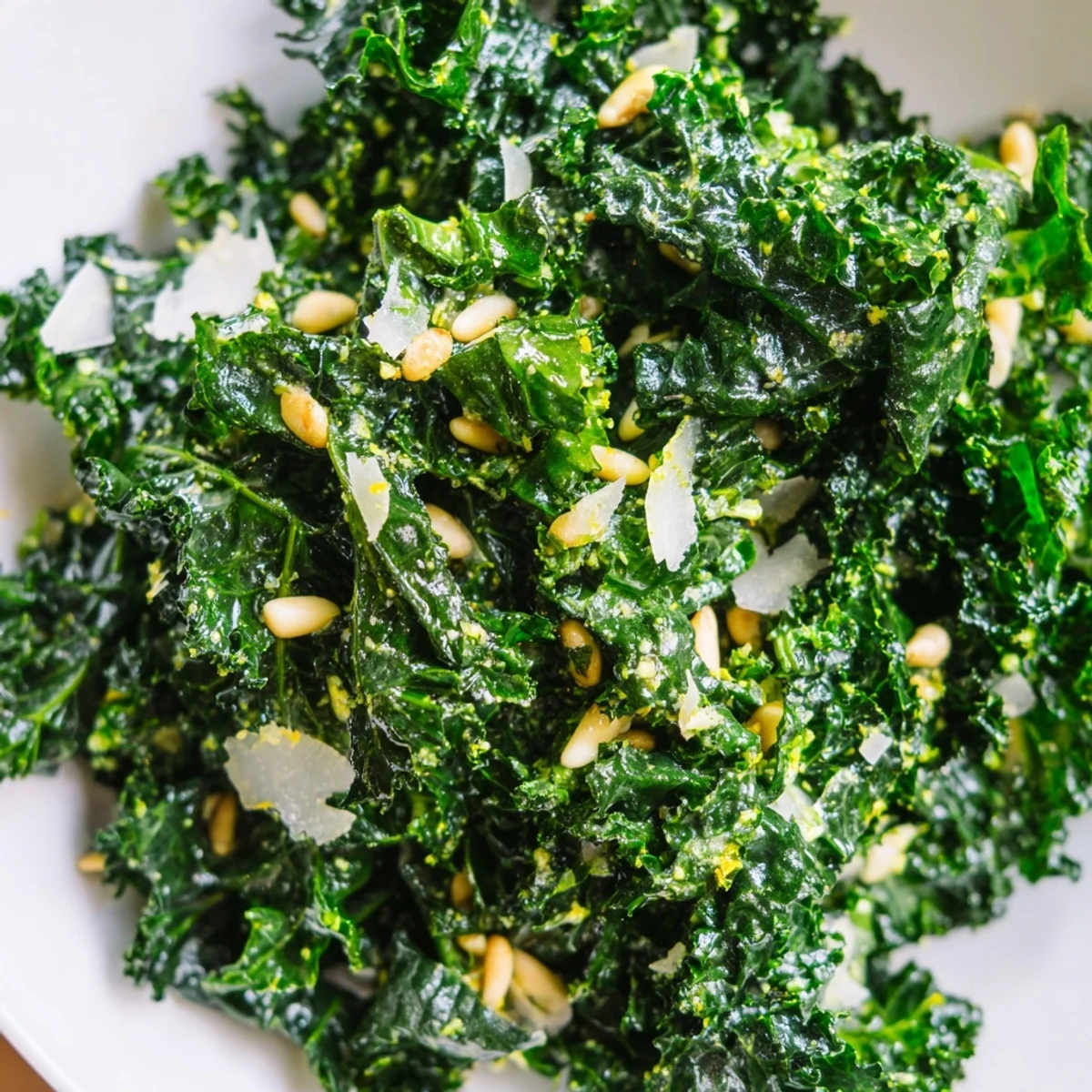 Crisp garlic lemon Parmesan kale salad in a wooden bowl with shaved cheese and toasted pine nuts