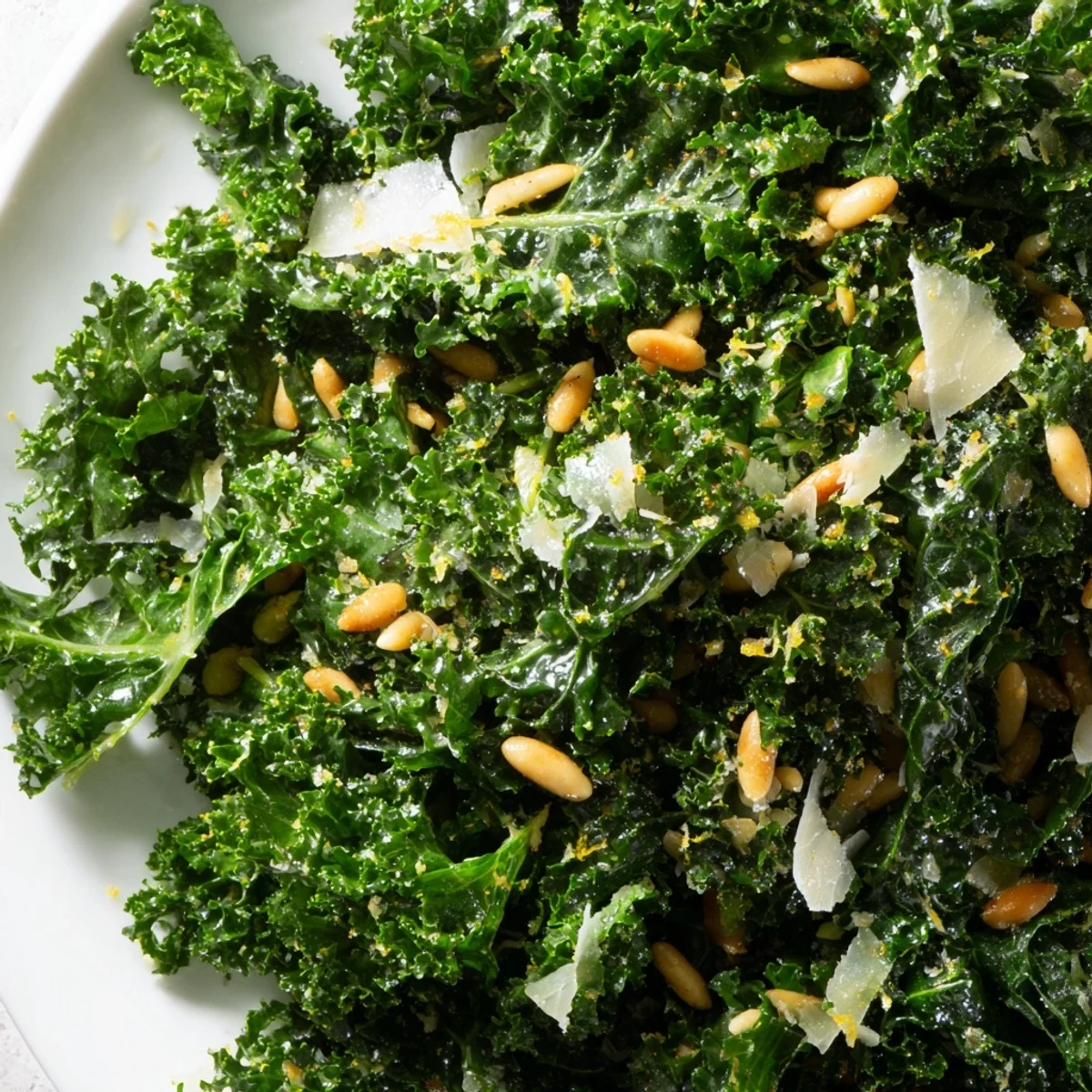 Massaged kale leaves glistening with zesty garlic lemon Parmesan dressing topped with crunchy nuts