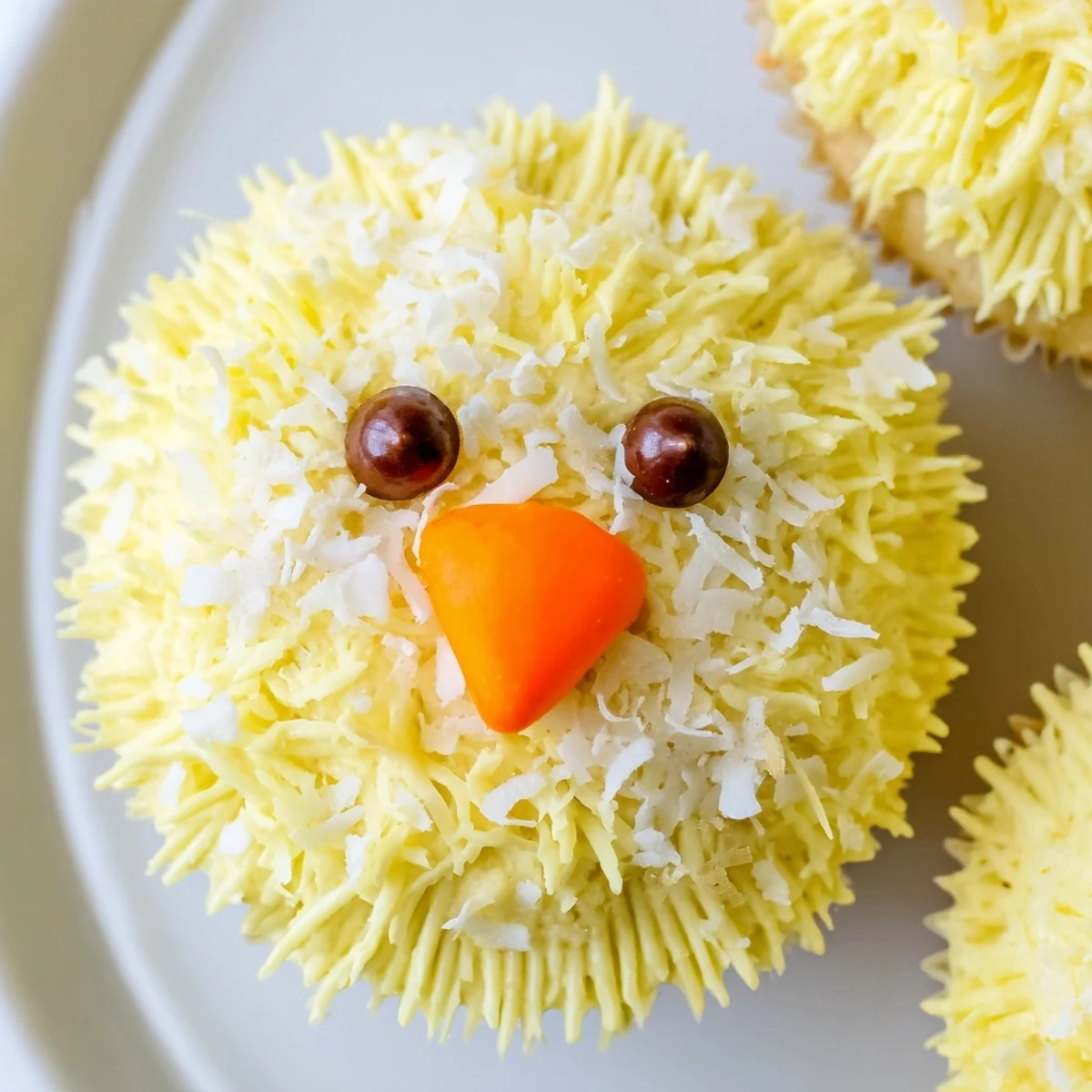 Adorable Easter Chick Cupcakes topped with coconut feathers and tiny chocolate chip eyes