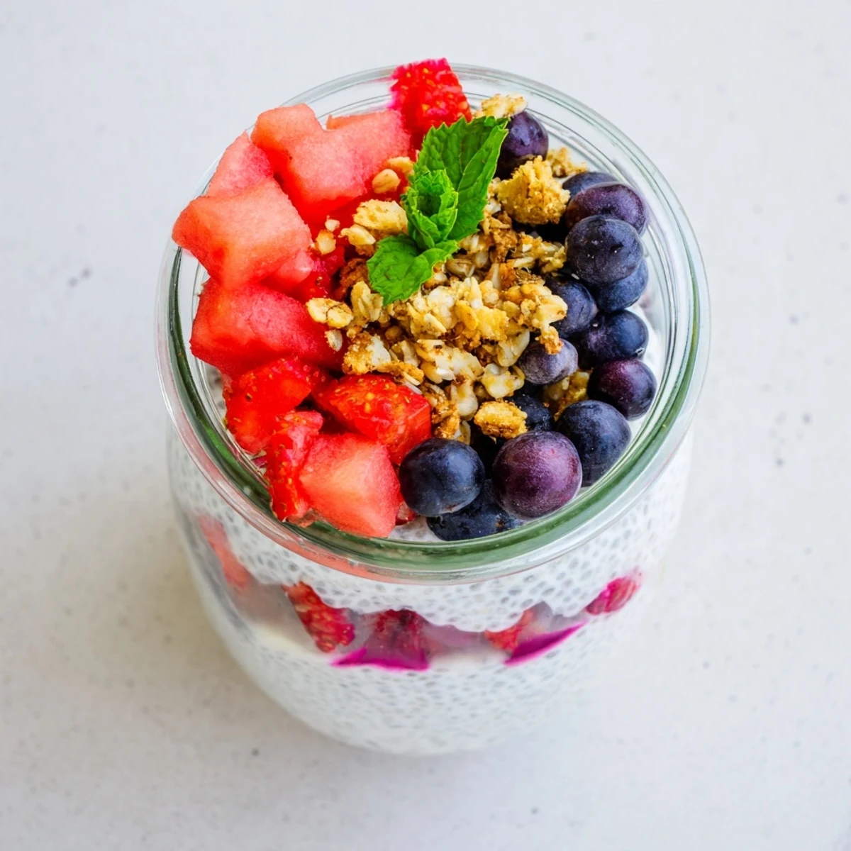 Refreshing watermelon chia parfait in clear glass with granola and green mint garnish