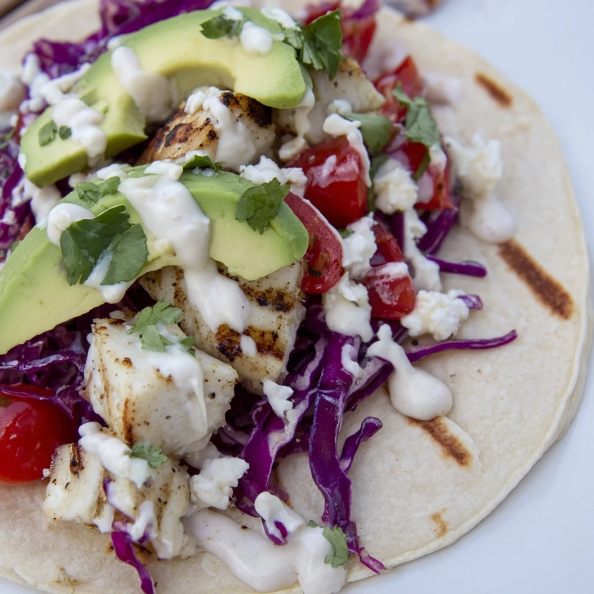 Charred white fish nestled in warm corn tortillas with vibrant red cabbage and creamy sauce