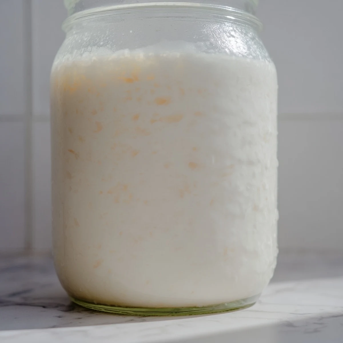 Fresh homemade coconut milk poured into a glass jar showcasing its creamy white texture