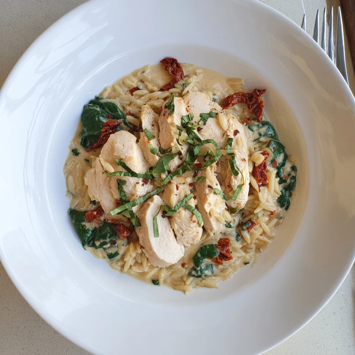 Creamy Marry Me Chicken Orzo in a white bowl topped with fresh basil and grated Parmesan cheese