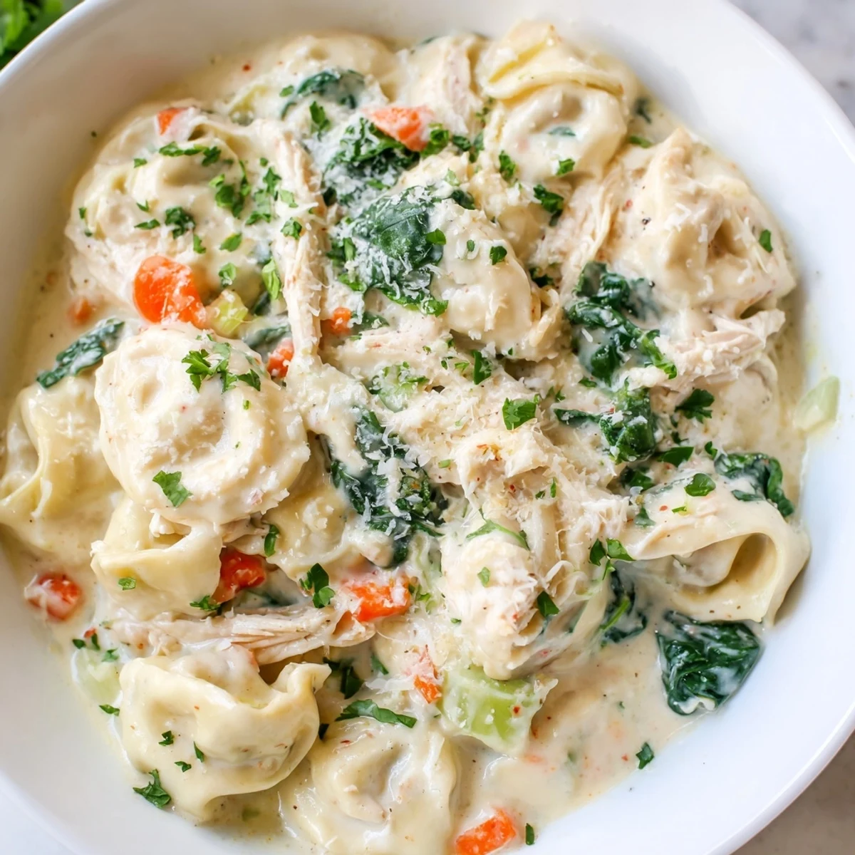 Creamy Crockpot Chicken Tortellini topped with Parmesan and fresh parsley in a white bowl