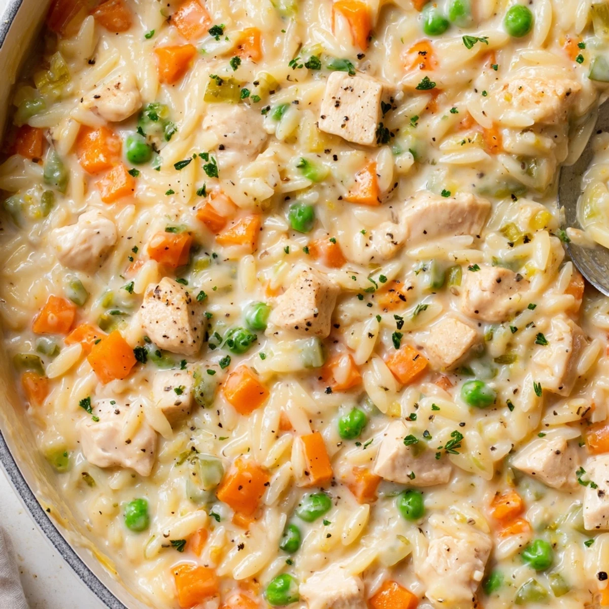 Steaming bowl of creamy chicken pot pie orzo loaded with colorful diced carrots and peas