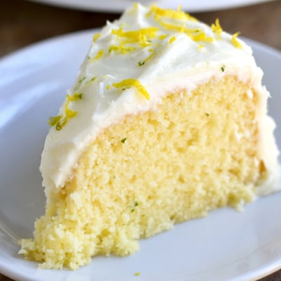 Golden Lemon Cake Slice with Frosting sits on a plate near a hot cup of tea.