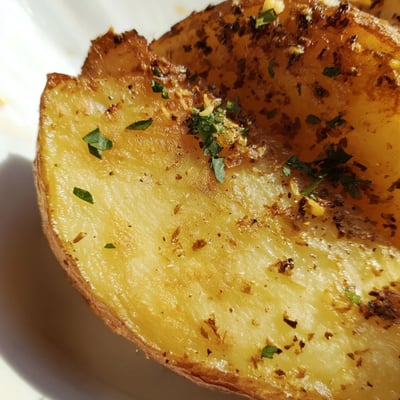 Roasted Lemon Potatoes glistening with olive oil and herbs, served alongside grilled chicken for a flavorful Greek-inspired meal.  