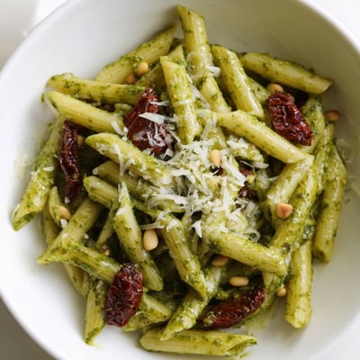 Creamy Green Pesto Pasta with Sun-Dried Tomatoes twirled on a fork, showcasing vibrant green sauce and rich tomato ribbons.
