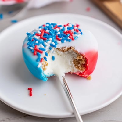 Handheld Fourth Of July Star Cheesecake Pops dipped in chocolate, sprinkled, chilled.