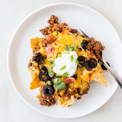 A layered Cheesy Nacho Casserole featuring spiced beef, warm beans, fresh cilantro.