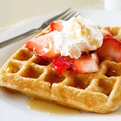 Plate of Strawberry Waffles Recipe topped with whipped cream and maple syrup